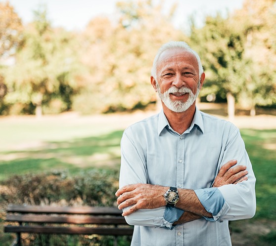 Senior man standing outside smiling with arms folded