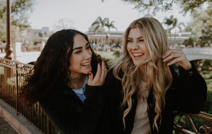 Two young women laughing together on a bridge