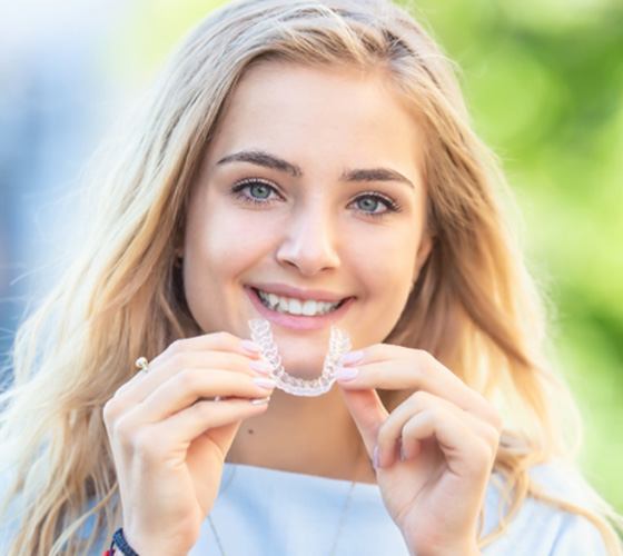 young woman smiling while holding Invisalign aligner