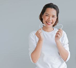Woman in white sweater smiling while holding Invisalign in Austin