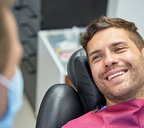 Man sitting in treatment chair and smiling at Invisalign dentist