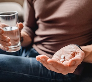 Man in brown sweater holding two pills and a glass of water