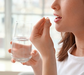 Profile nose-down view of woman taking a pill with a glass of water in front of window