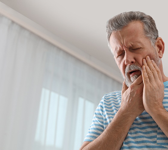 Man in striped shirt rubbing jaw in pain