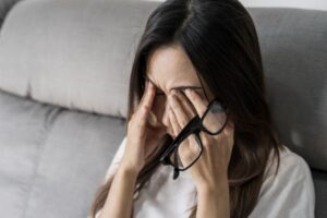Woman sitting on sofa, experiencing eye pain 